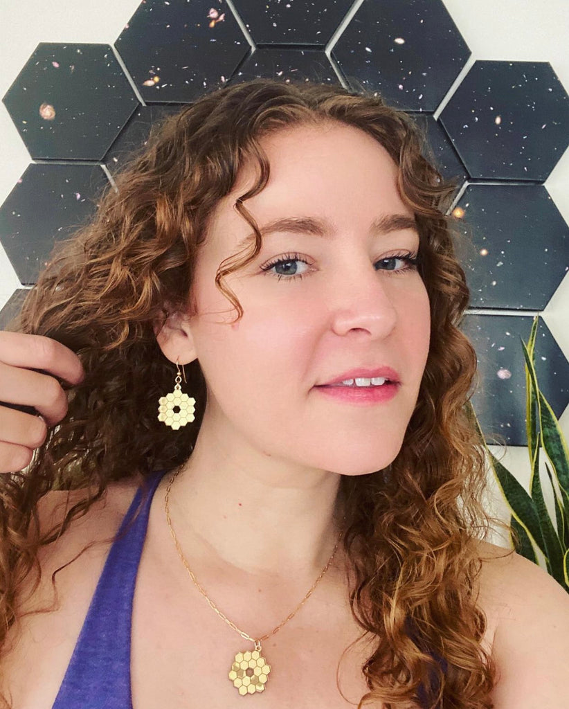 Scientist wearing gold JWST necklace and James Webb earrings with 18 hexagons in the background